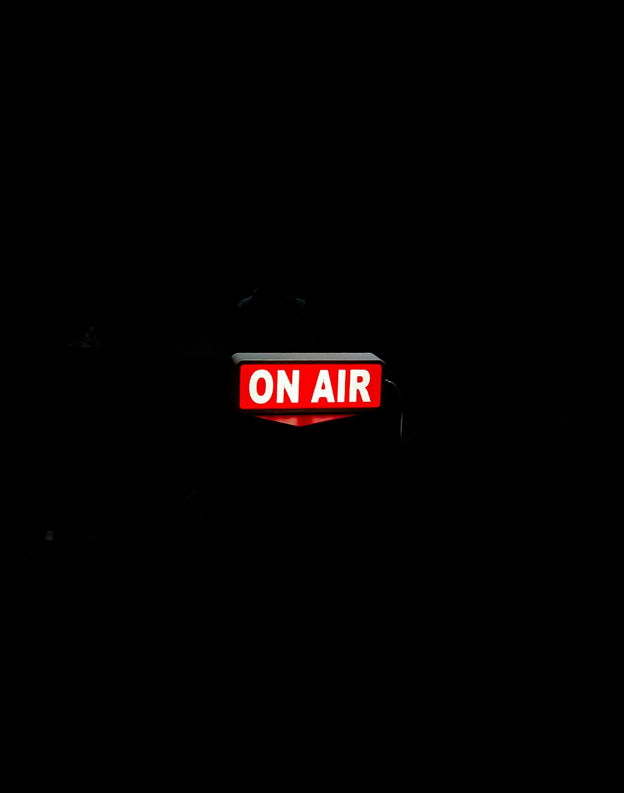 Bright 'On Air' sign glows in dark studio, creating moody atmosphere.