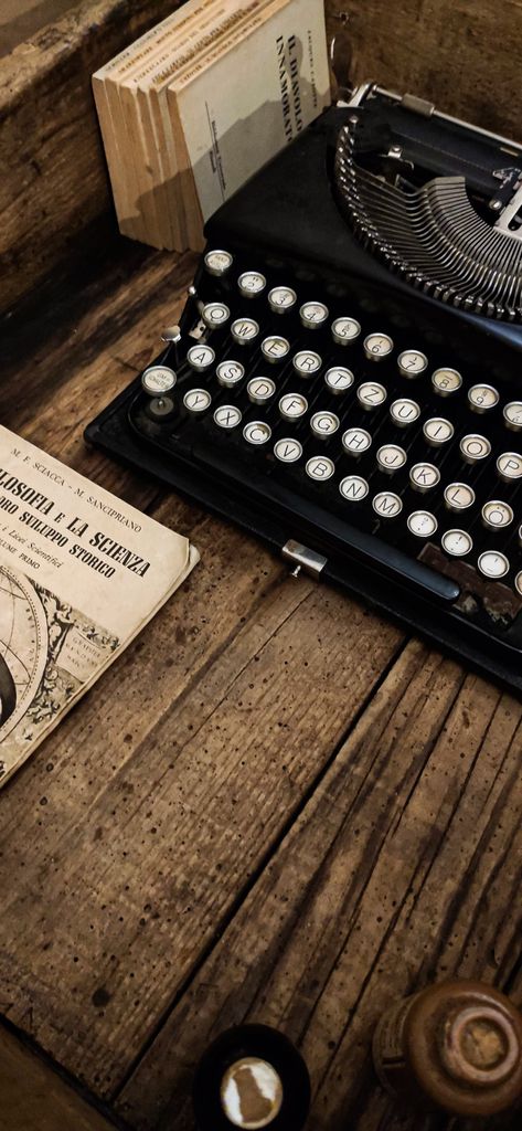 Close-up of an antique typewriter and old books on wooden surface, evoking a vintage writing atmosphere.